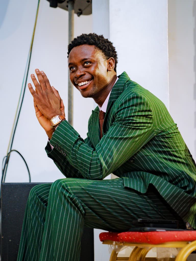 Precious Alo seated and smiling during a gathering, hands clasped